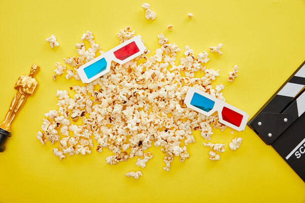 KYIV, UKRAINE - AUGUST 13, 2019: top view of popcorn, 3d glasses and clapper board with golden Oscar statuette on yellow background