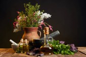 agyag váza, friss fűszernövények és virágok közelében habarcs és zúzás és palackok fából készült asztal izolált fekete