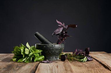 mortar with pestle near fresh green and purple basil on wooden table isolated on black clipart