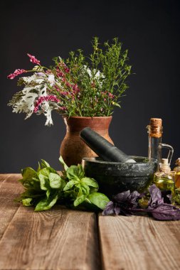 grey mortar near clay vase with fresh and herbs on wooden table isolated on black clipart