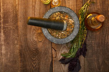top view of mortar with pestle near fresh herbs and bottles on wooden surface with copy space clipart