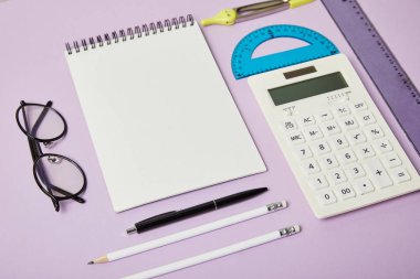 rulers and calculator near notebook and glasses isolated on purple  clipart