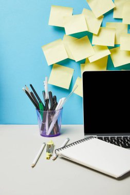 Yapışkan notların yanında boş ekranlı bir laptop, mavi ve beyaz üzerine gözlük ve kırtasiye malzemesi 