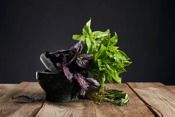 黒で隔離された木製のテーブルの上にローズマリーと新鮮な緑と紫のバジルとモルタル — ストック写真