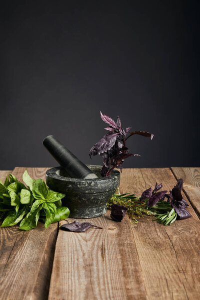 grey mortar with pestle near fresh green and purple basil on wooden table isolated on black