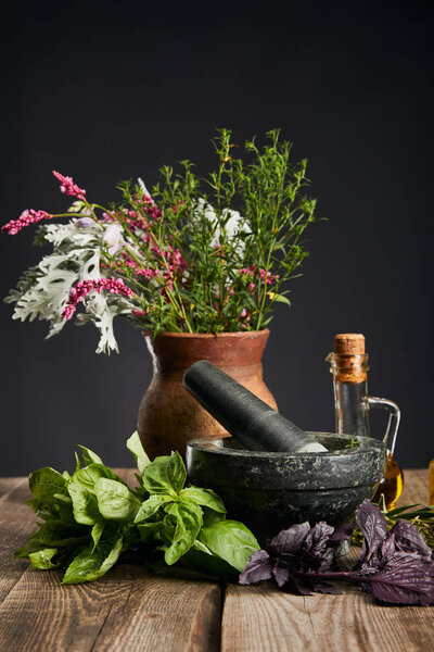 grey mortar, clay vase with herbs and bottle on wooden table isolated on black