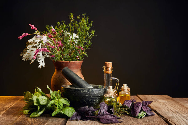 grey mortar near clay vase with fresh wildflowers and herbs on wooden table isolated on black