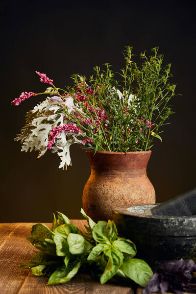 clay vase with fresh wildflowers and herbs on wooden table isolated on black