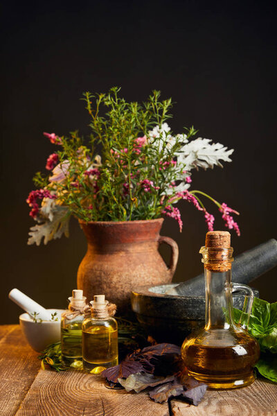 clay vase with fresh herbs and flowers near mortar and pestle and bottles on wooden table