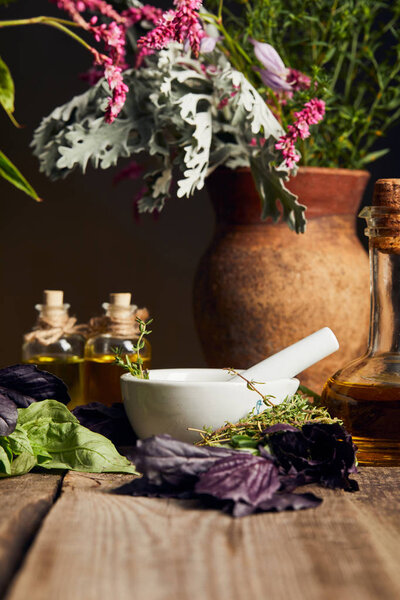 mortar with pestle near bottles with oil and vase with fresh flowers on wooden surface isolated on black