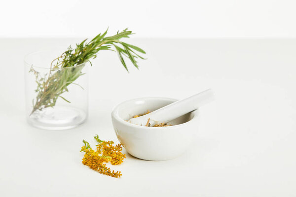 mortar and pestle with herbal mix and and glass with fresh plants on white background