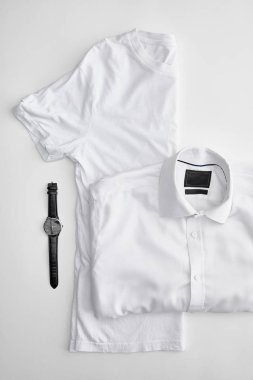 top view of folded in half t-shirt near plaid shirt and watches on white background clipart