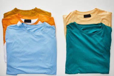 top view of beige, orange, blue, turquoise and ochre t-shirts on white background clipart