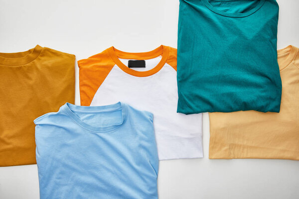 top view of beige, orange, blue, turquoise and ochre folded t-shirts on white background