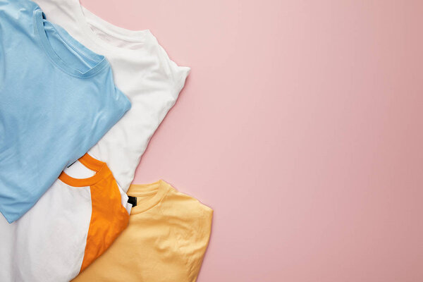 top view of white, yellow, orange and blue folded t-shirts on pink background
