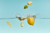 reife Zitronen- und Limettenstücke fallen tief ins Wasser mit Spritzer auf blauem Hintergrund