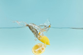 řezané citrony hluboko ve vodě s šplouchnutím na modrém pozadí