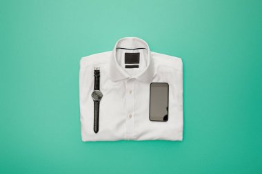 turkuaz arka plan üzerinde düz beyaz katlanmış gömlek üzerinde saatler ve akıllı telefon üst görünümü