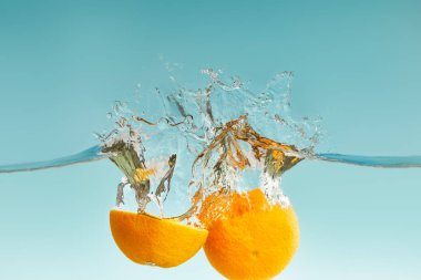 ripe cut orange falling in water with splashes on blue background clipart