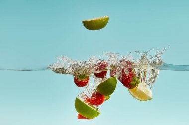 ripe lime pieces and strawberries falling deep in water with splash on blue background clipart
