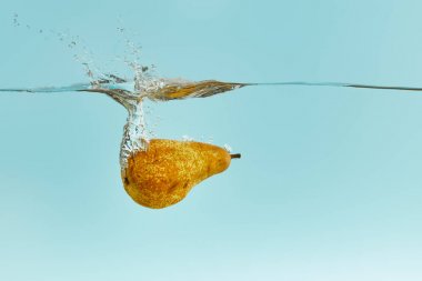 ripe pear falling deep in water with splash on blue background clipart