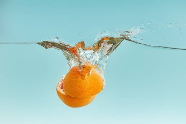 fresh orange halves falling in water on blue background clipart