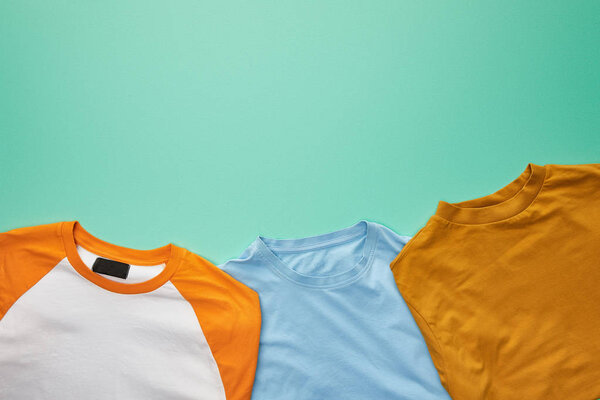 top view of folded orange, blue and ochre t-shirts on turquoise background