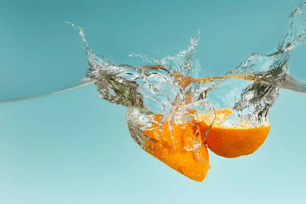 Mitades Naranjas Maduras Cayendo Agua Con Salpicaduras Sobre Fondo Azul — Foto de Stock