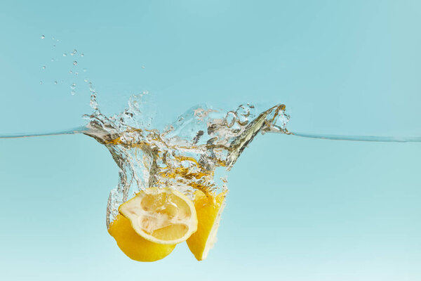 yellow ripe lemons falling deep in water with splash on blue background