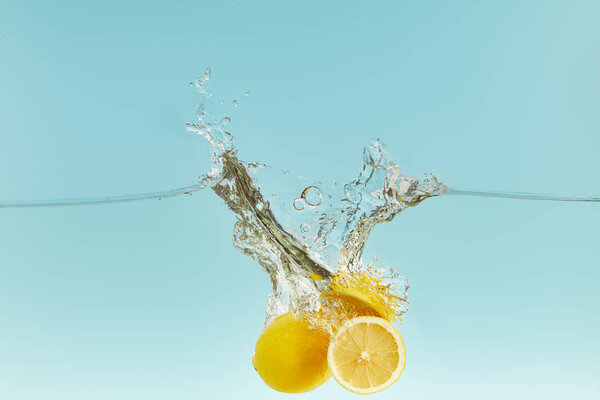 ripe lemons falling deep in water with splash on blue background