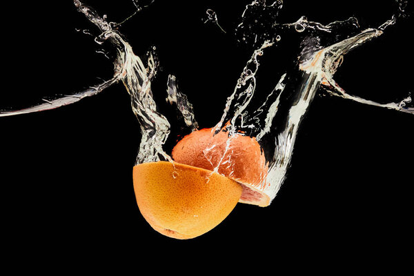 ripe grapefruit halves falling in water with splash isolated on black