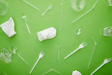 yeşil arka plan üzerinde tek kullanımlık plastik bardak, çatal ve kaşık üst görünümü