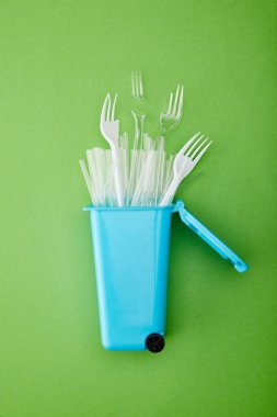 yeşil arka plan üzerinde kırık plastik çatal ve pipetler ile mavi geri dönüşüm kutusu üst görünümü