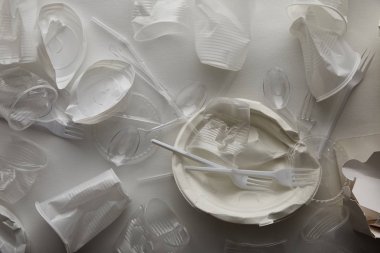 top view of crumpled disposable plates, plastic cups, forks and spoons on white background  clipart
