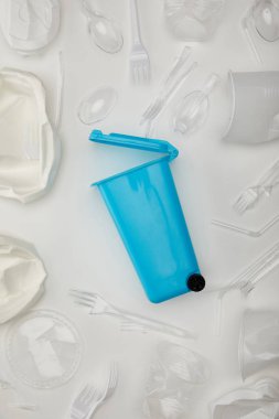 top view of blue recycle bin, crumpled disposable cups, forks, spoons and plate on white background clipart