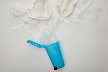 beyaz arka plan üzerinde buruşturulmuş plastik bardak, tabak, çatal ve kaşık ile mavi geri dönüşüm kutusu üst görünümü