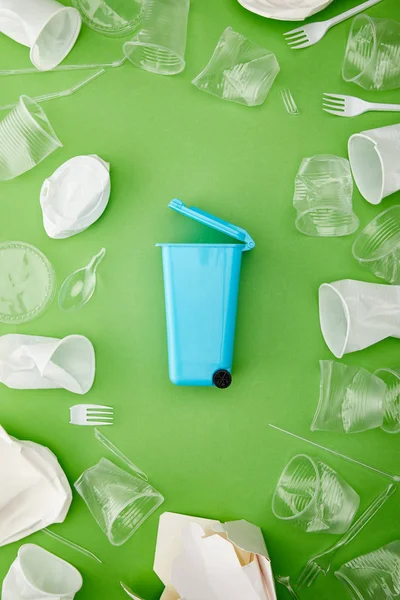 緑の背景にくしゃくしゃのプラスチックカップの間の青いごみ箱の上のビュー — ストック写真