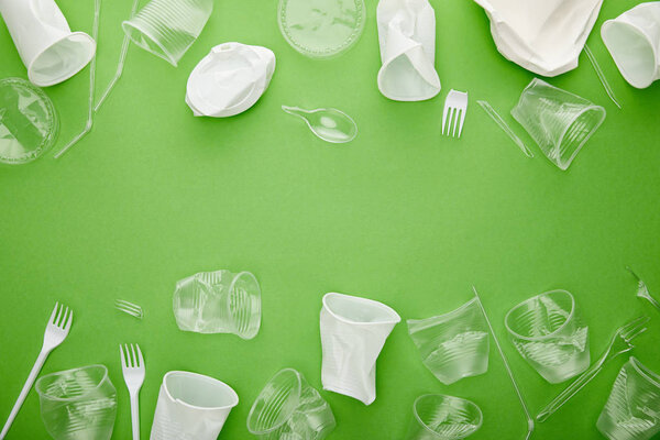 top view of crumpled plastic cups, forks and plates on green background with copy space 