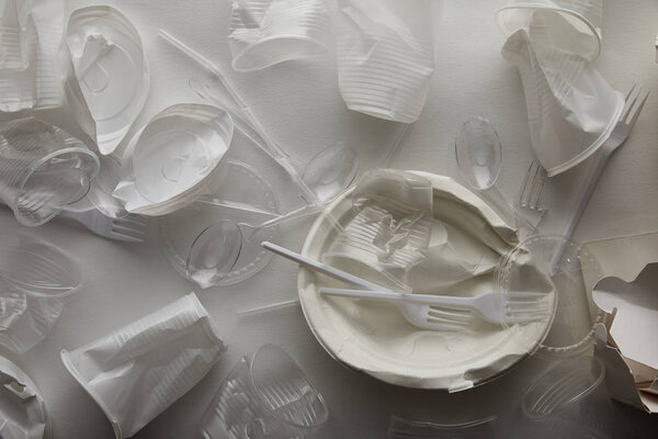 top view of crumpled disposable plates, plastic cups, forks and spoons on white background 
