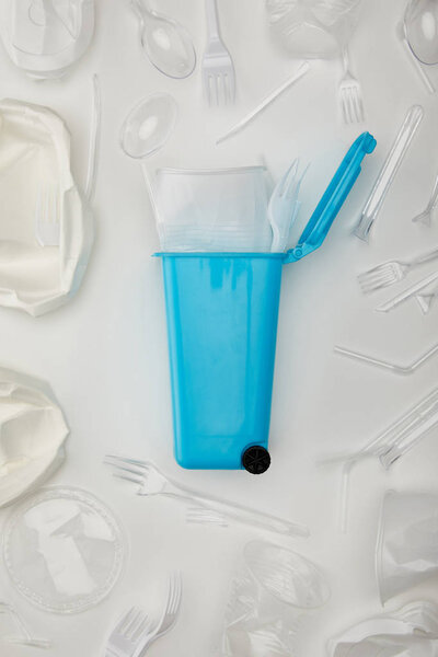 top view of blue recycle bin with crumpled disposable cup, fork, spoons and plates on white background