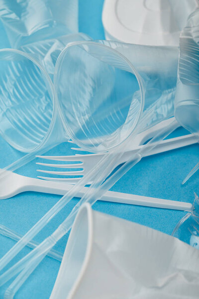 pile of crumpled plastic cups and forks on blue background