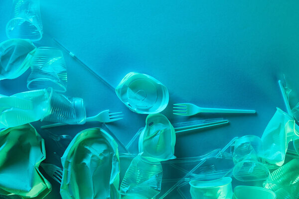 top view of crumpled plastic cups, straws and forks with copy space in blue light