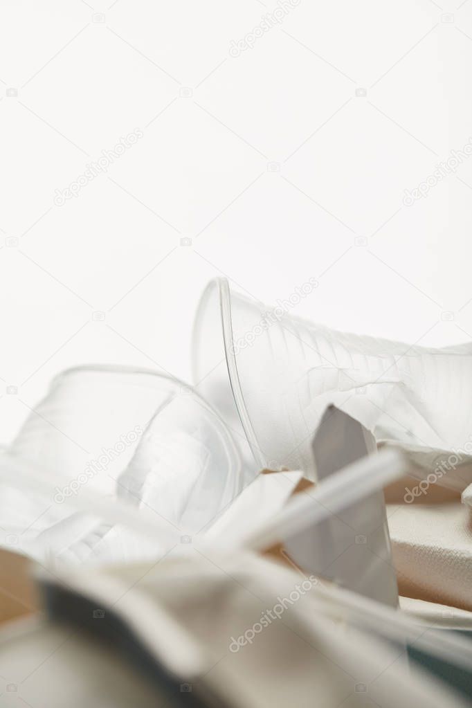 close up view of transparent plastic cups in pile of rubbish on white background