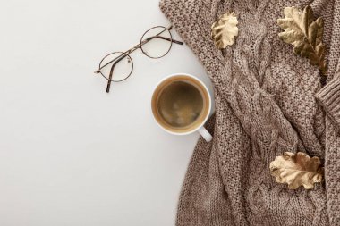 top view of knitted brown sweater, glasses, coffee and golden foliage on white background clipart