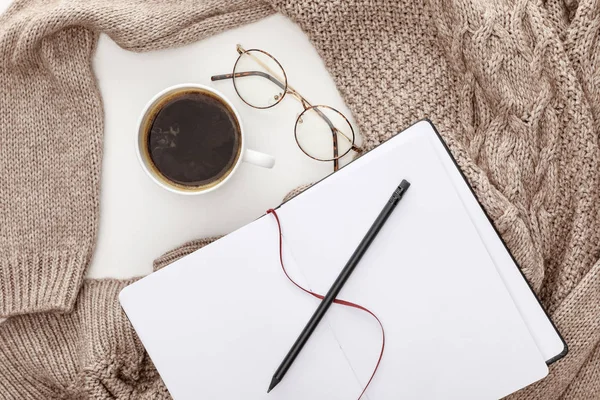 白い背景に空のノートブック ニットブラウンのセーター コーヒーとメガネのトップビュー — ストック写真