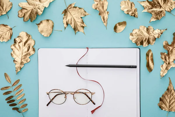 青い背景にメガネをかけた空白のノートブックの近くに秋の黄金の葉を持つ平らな横たわる — ストック写真