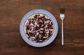 top view of fork near striped plate with raw beans on wooden table
