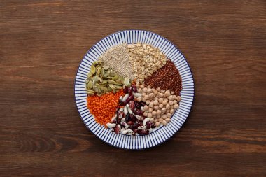 ahşap masa üzerinde çiğ mercimek, nohut, Kinoa, yulaf ezmesi, fasulye ve kabak çekirdeği ile çizgili plaka üst görünümü