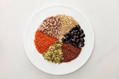 mermer yüzeyinde çiğ mercimek, Quinoa, yulaf ezmesi, fasulye ve kabak çekirdeği ile beyaz plaka üst görünümü