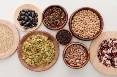 top view of wooden bowls with diverse beans, quinoa, peppercorns, pumpkin seeds and chickpea on white marble surface clipart